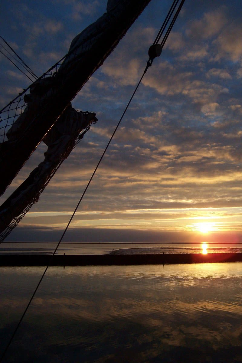 Sonnenuntergang über dem Wasser mit Schiffsmast